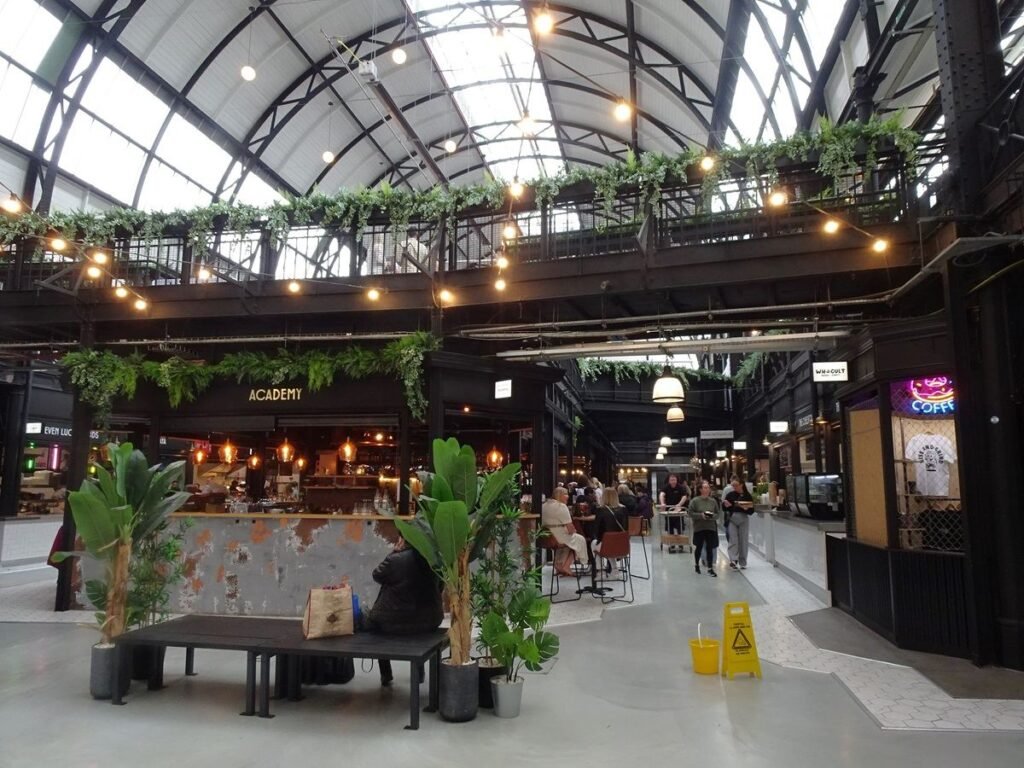 Indoor Market Halls Win Back Weekend Food Shoppers Stalls inside a bright indoor market hall selling fresh produce, bread, and flowers.